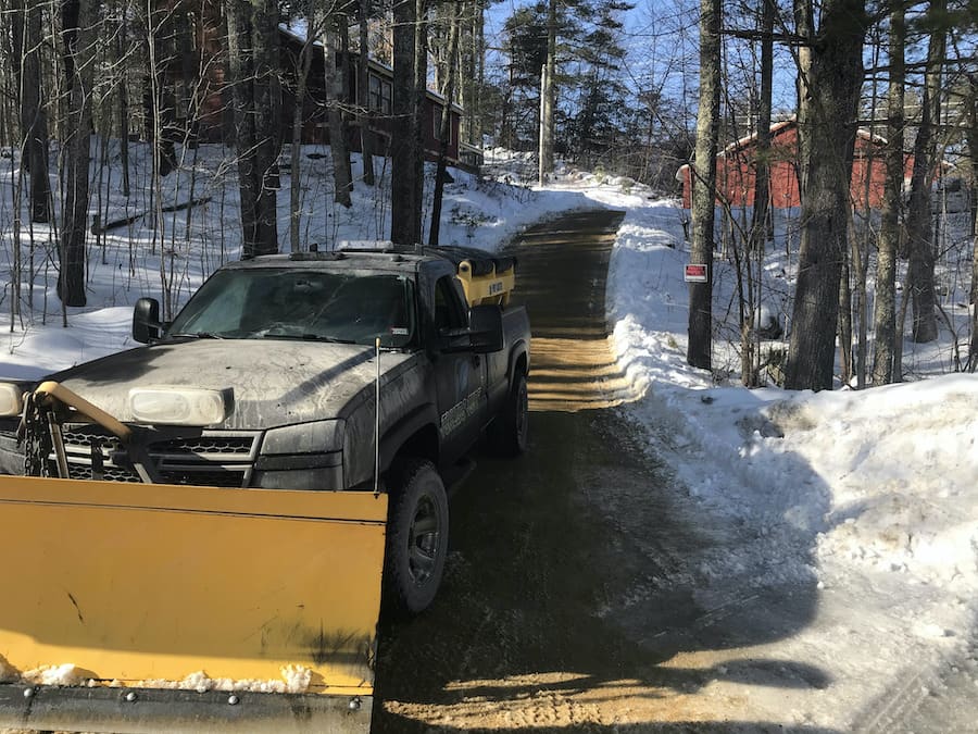 Truck with plow at the end of a long driveway in winter