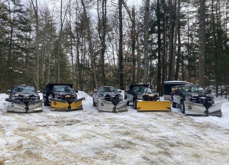 Snow plowing trucks parked in a line on a winter day in front of the woods